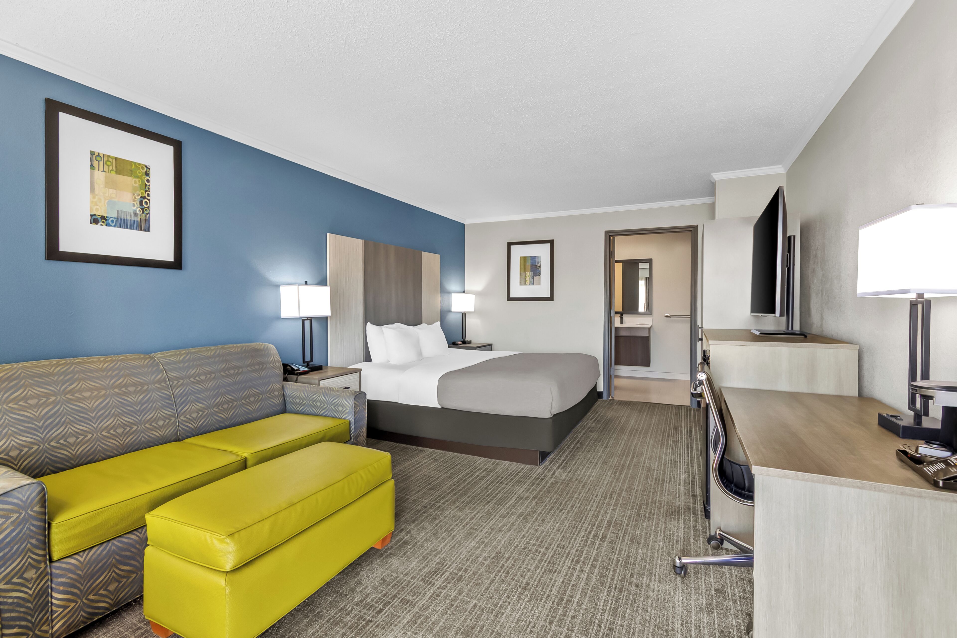 A hotel room with a bed, a sofa, a desk, and a television.