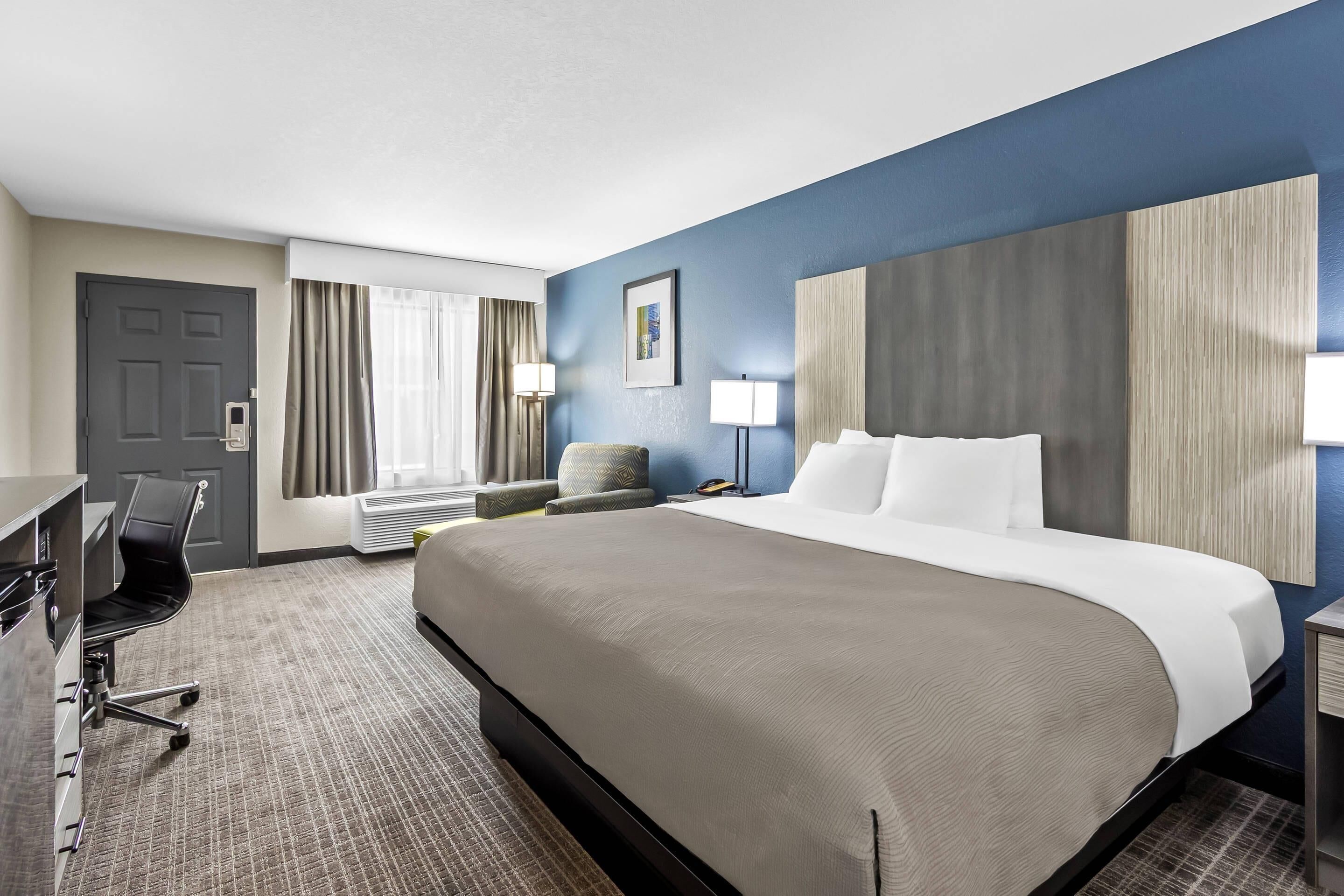 A hotel room with a bed, desk, chair, and a large window with curtains.