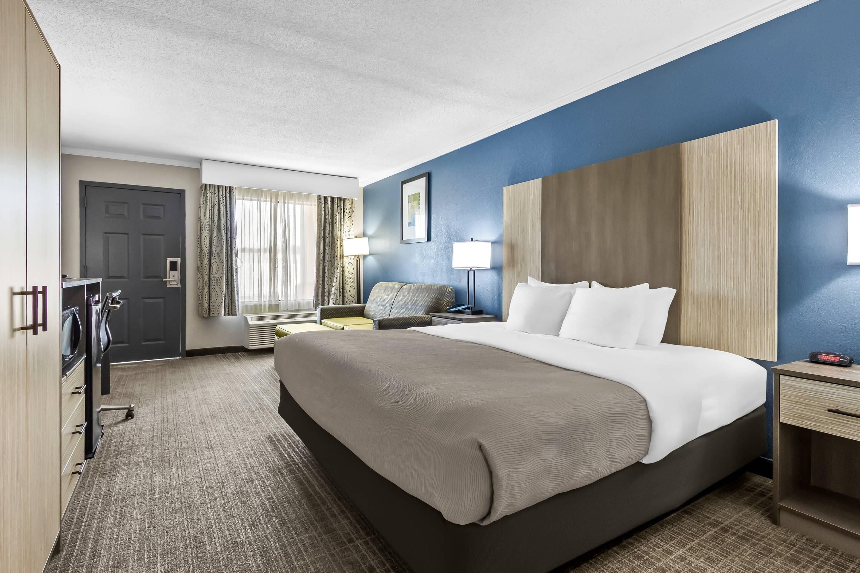 A hotel room with a large bed, a desk, a chair, a wardrobe, and a door.