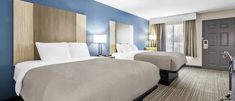 A hotel room with two beds, a desk, a chair, a lamp, a door, and a window with curtains.