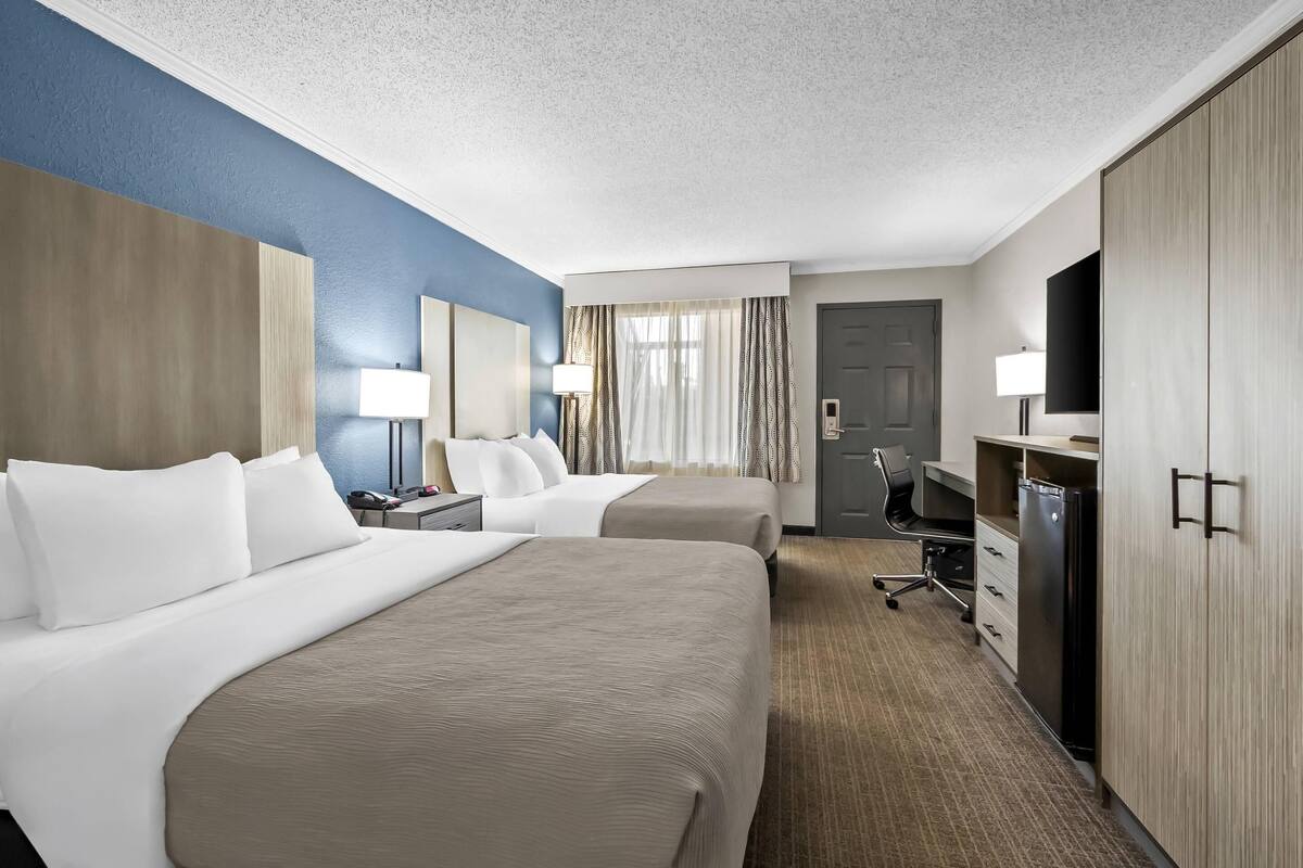 A hotel room with two beds, a desk, a TV, and a wardrobe.