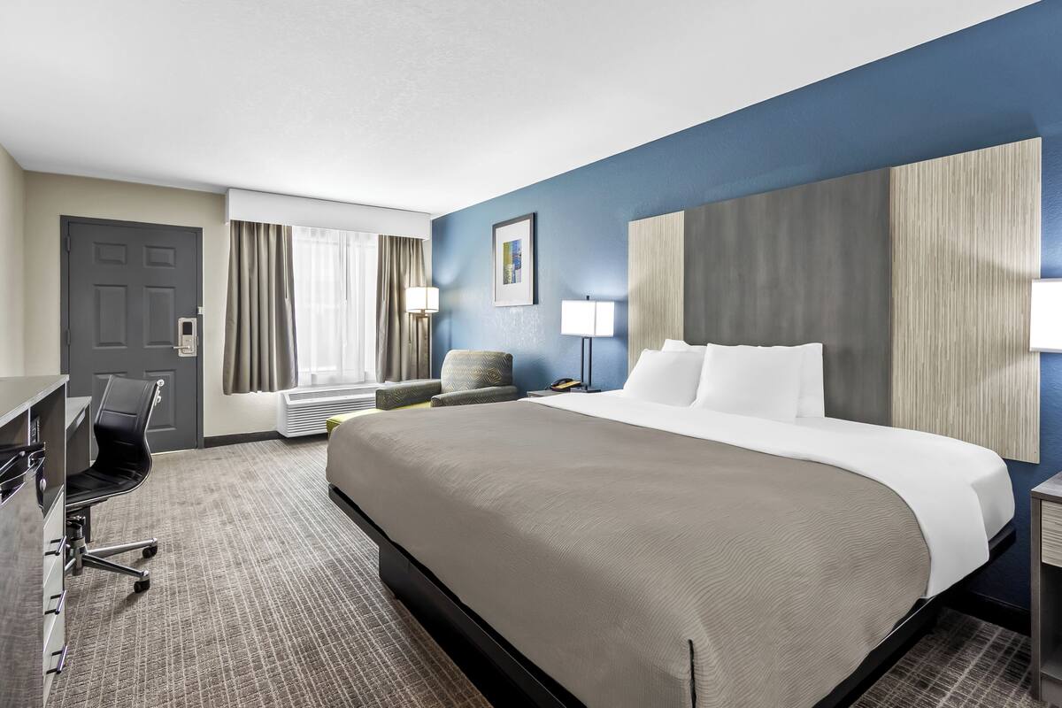 A hotel room with a large bed, a desk, a chair, a lamp, and a window with curtains.