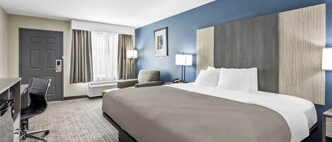 A hotel room with a large bed, a desk, a chair, a lamp, and a window with curtains.