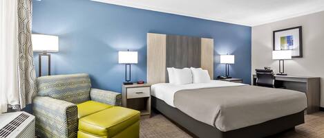 A hotel room with a bed, a desk, a chair, a lamp, and a radiator.