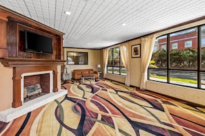 A hotel room with a fireplace, a television, a sofa, a patterned carpet, and large windows offering a view of the outside. - Quality Inn & Suites Florence Civic Center (Florence)