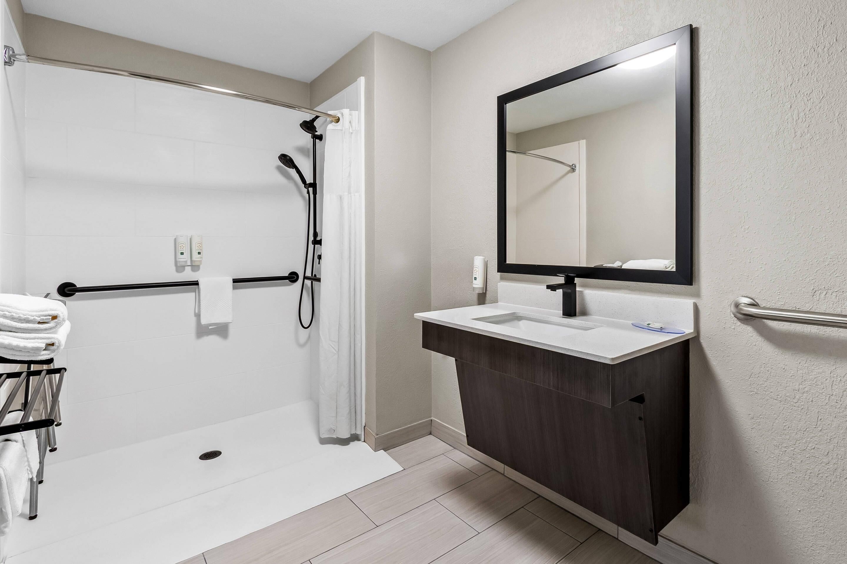 A modern bathroom with a walk-in shower, a sink with a dark vanity, and a large mirror.