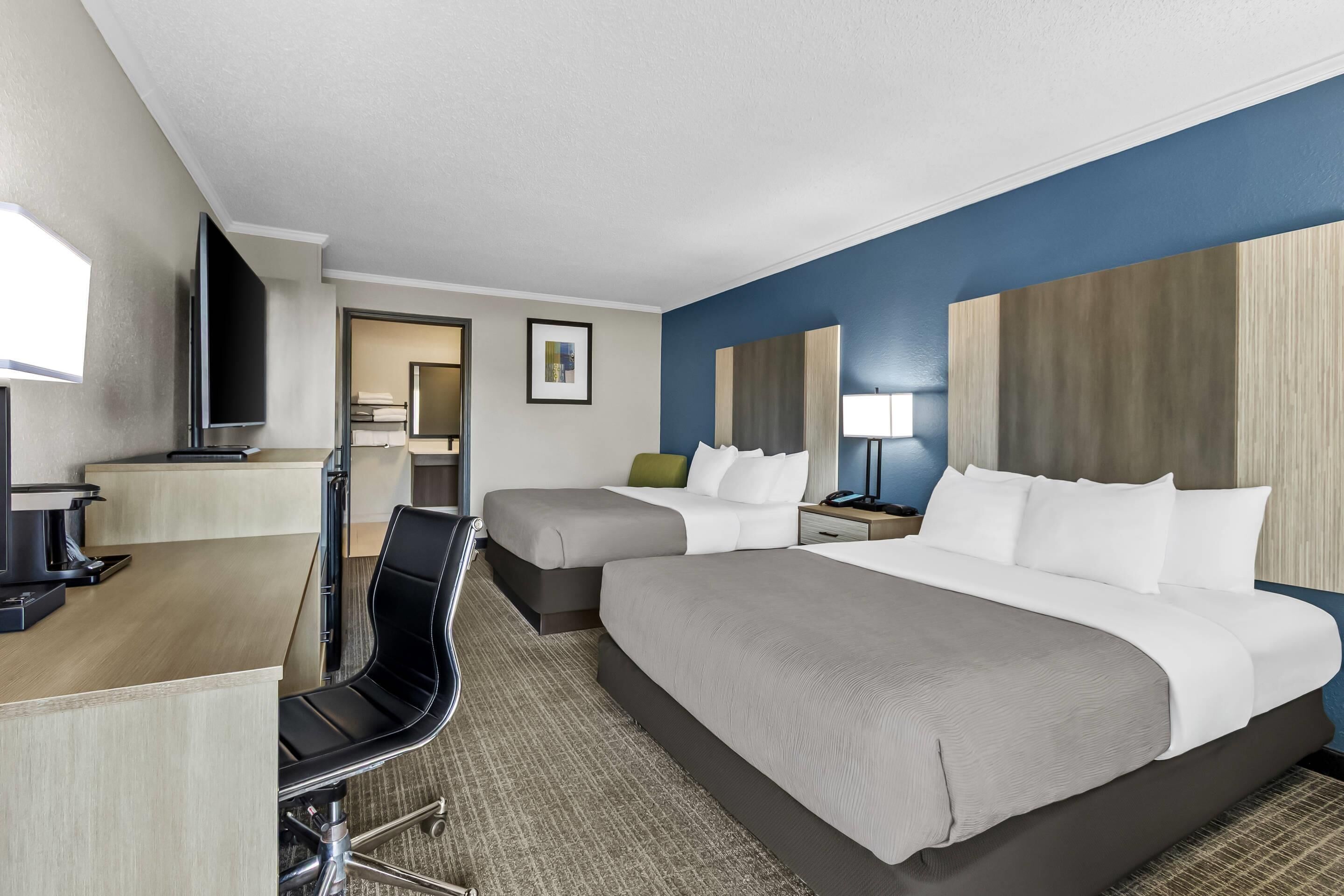 A hotel room with a bed, a desk, a chair, a TV, and a bathroom visible through an open door.