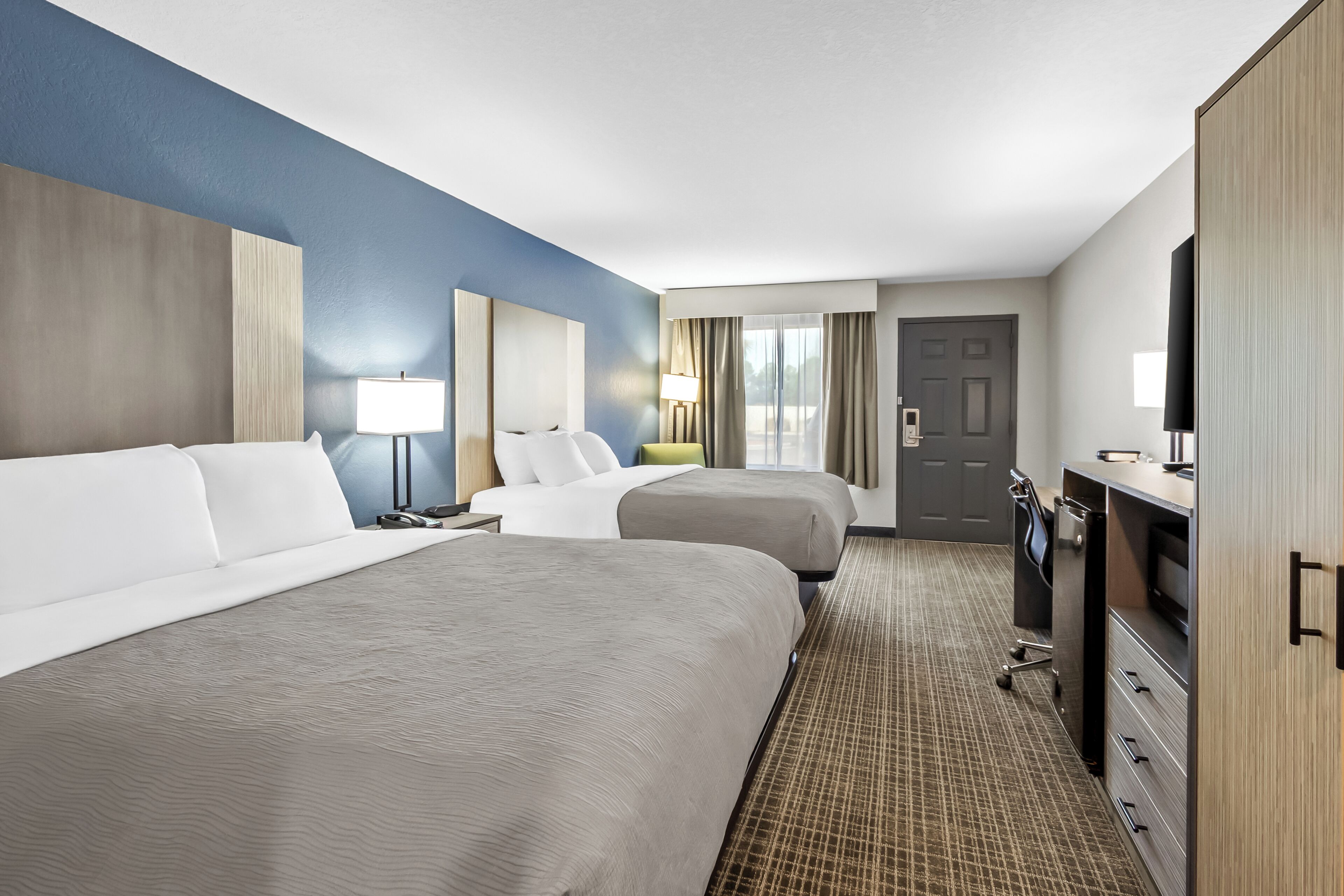 A hotel room with two beds, a desk, a TV, and a wardrobe.