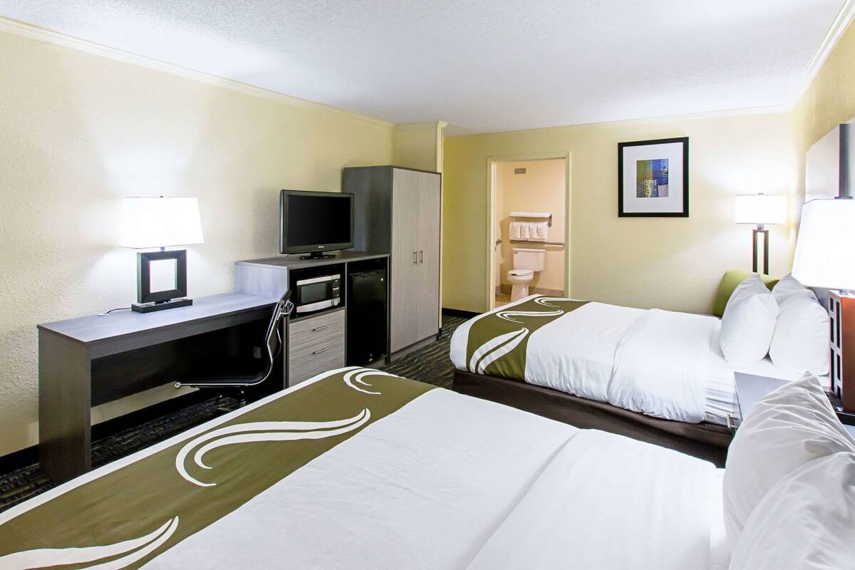 A hotel room with two beds, a desk with a computer, a television, a microwave, and a cabinet.