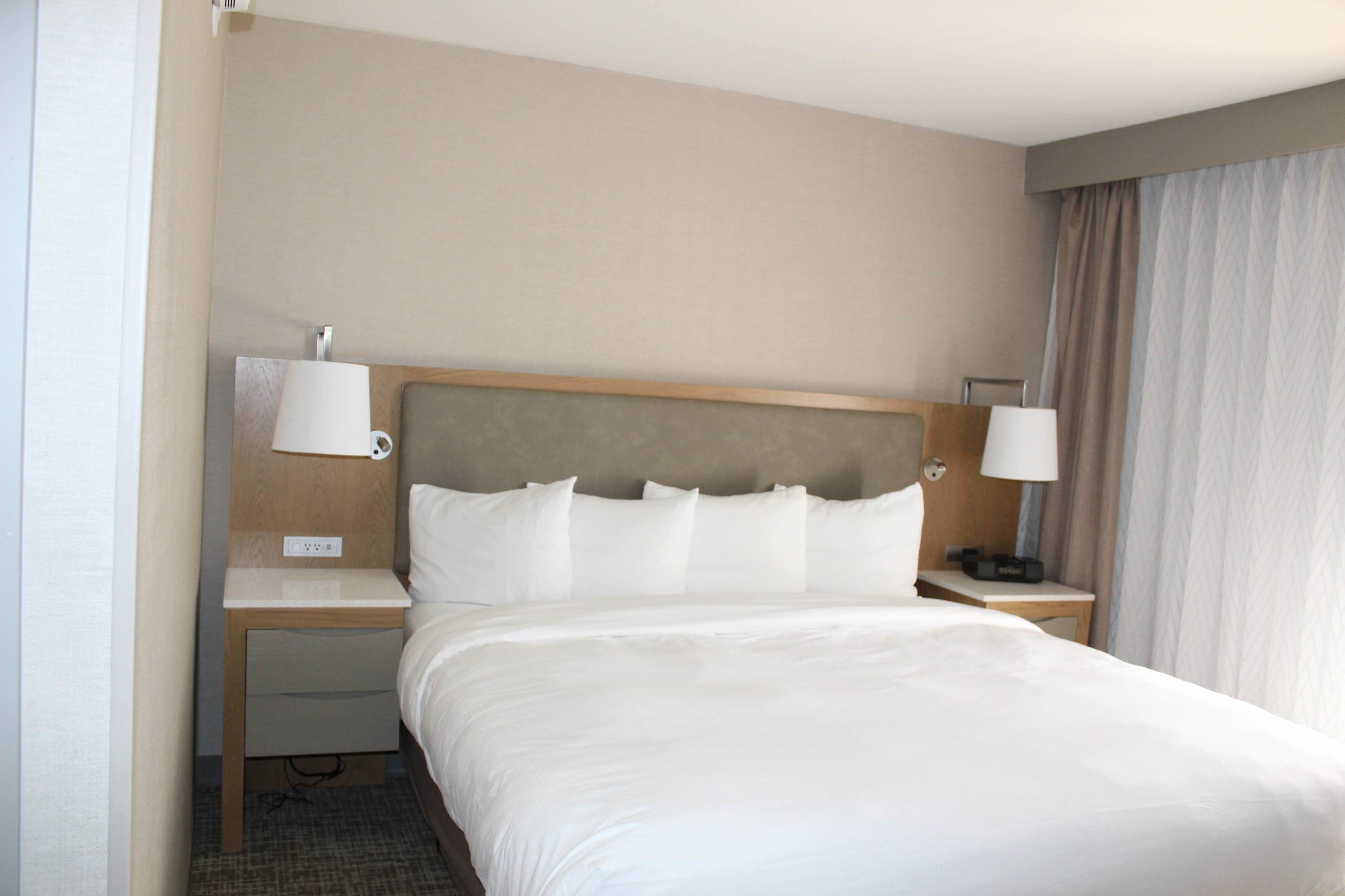 Una habitación de hotel con una cama grande, dos mesitas de noche, una lámpara y un enchufe.