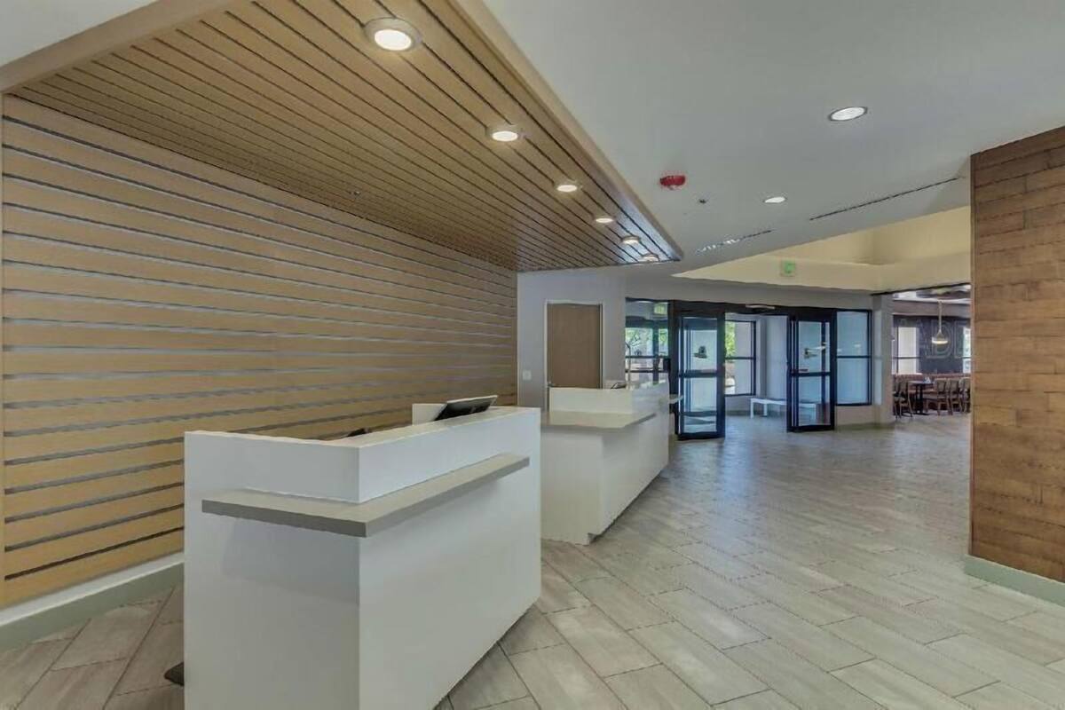 A reception area with a wooden slat wall, white reception desk, and a spacious interior with a tiled floor.
