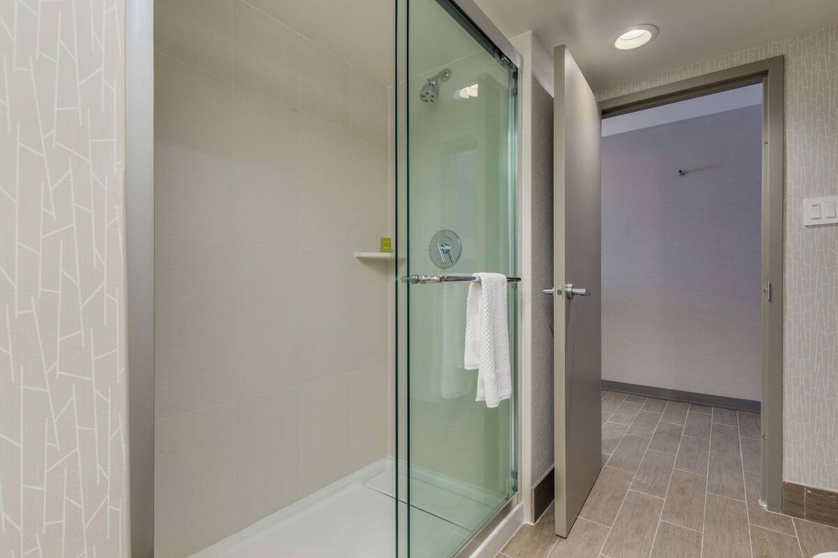 A modern bathroom with a glass shower enclosure, a white towel hanging on the door, and a tiled floor.