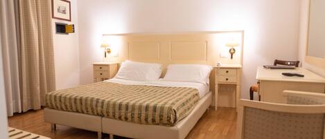 A hotel room with a bed, bedside tables, a desk, a chair, and a mirror.