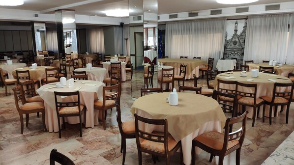 Un salón de banquetes con mesas redondas y sillas, dispuesto en un amplio espacio.