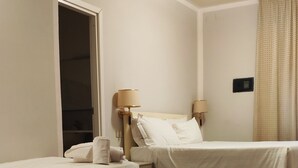 A hotel room with two beds, a wooden floor, a door, and a wall-mounted light fixture. - Grand Hotel Duomo (Pisa)
