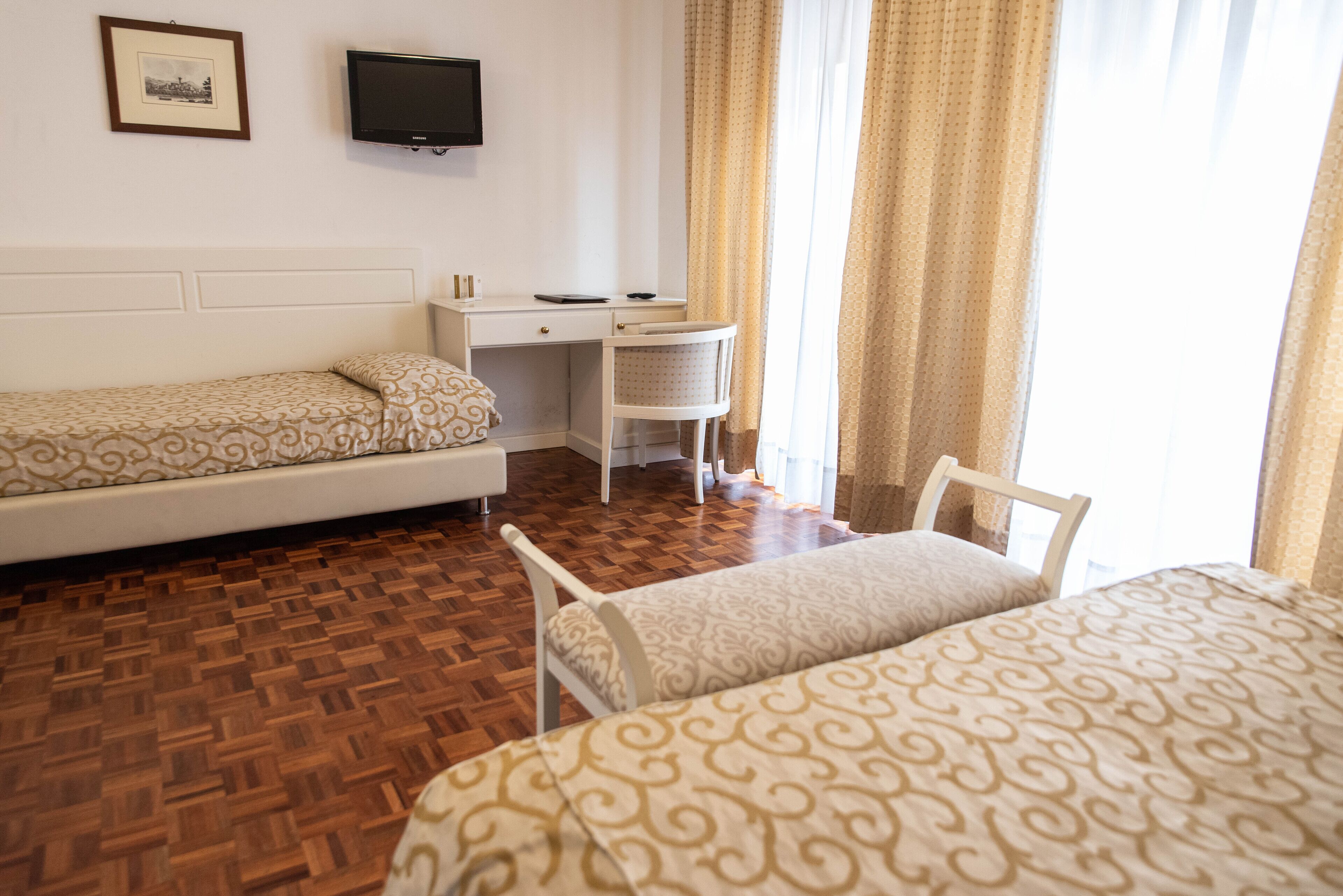 Habitación de hotel con dos camas individuales, un escritorio, una silla, un televisor y una ventana con cortinas.