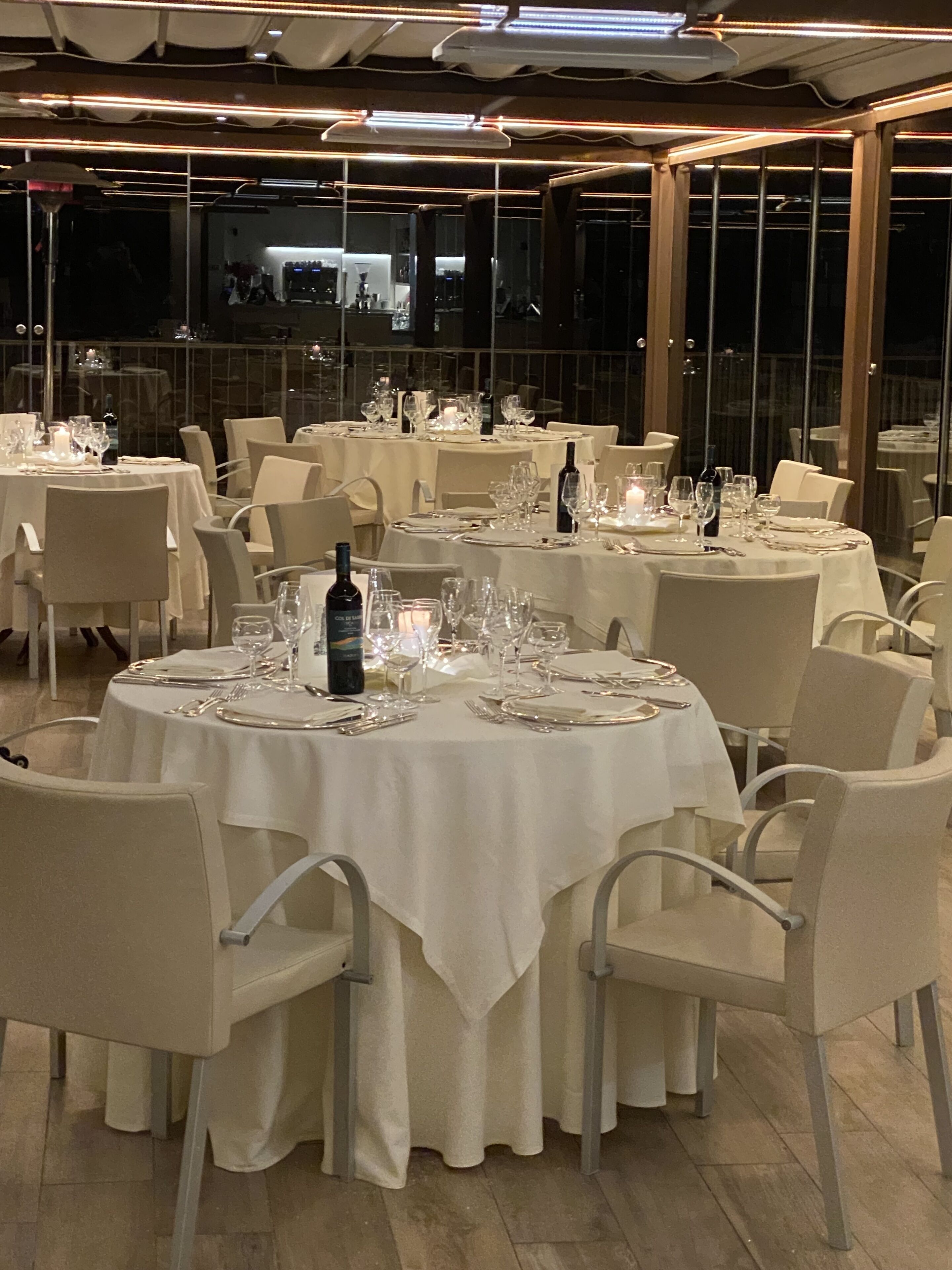Un restaurante con mesas redondas dispuestas para comer, sillas y mesas cubiertas con manteles blancos.
