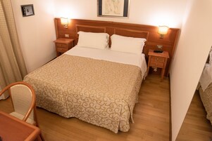 Una habitación de hotel con una cama grande, dos mesitas de noche, una silla y un cabecero de madera.
