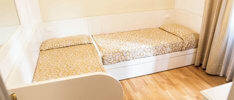 A small, single-bed room with a wooden floor, white walls, and a patterned bedspread.