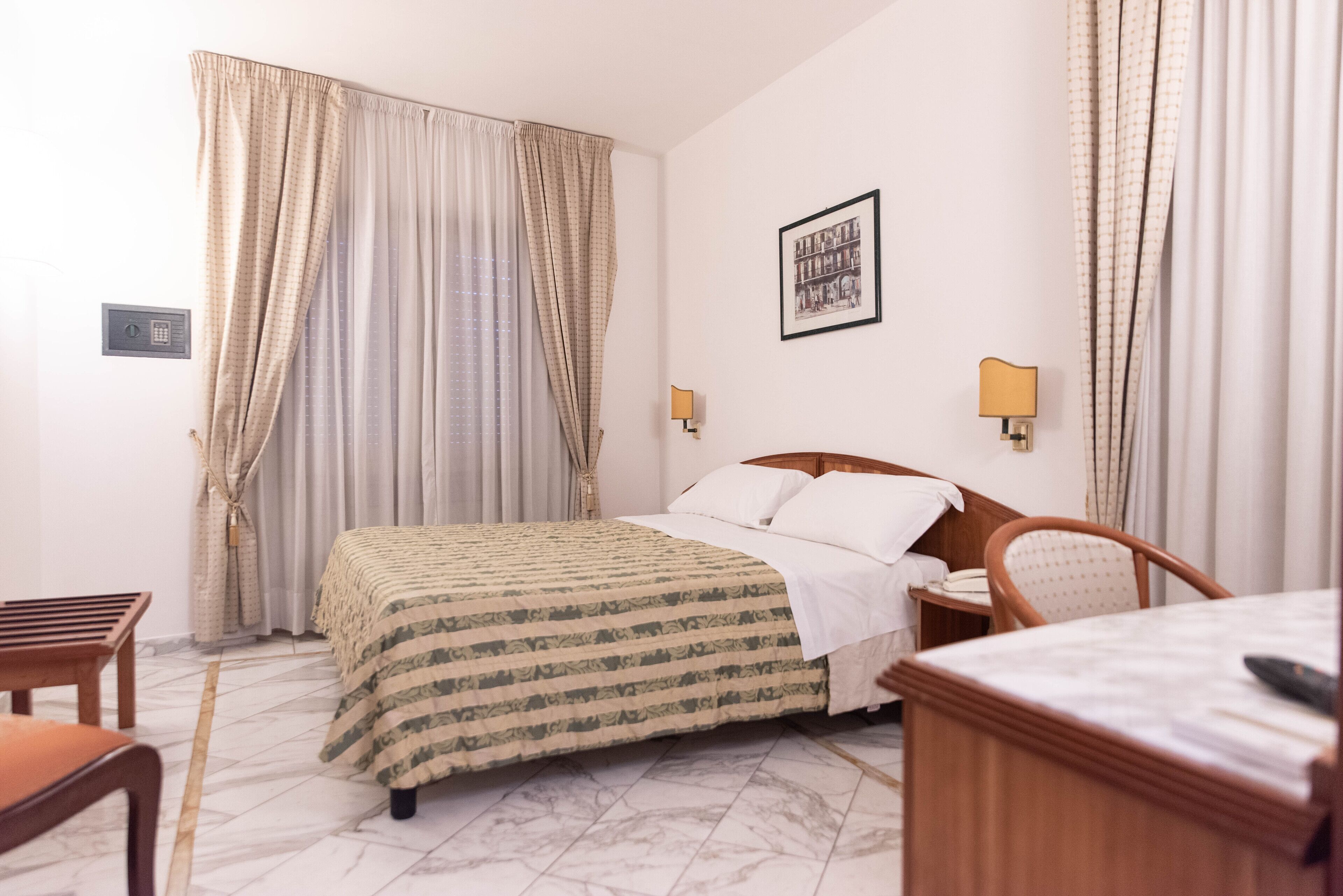 A hotel room with a bed, a chair, a desk, and a lamp.