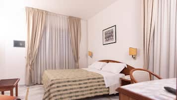A hotel room with a bed, a chair, a desk, and a lamp.