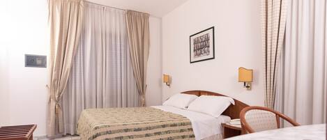 A hotel room with a bed, a chair, a desk, and a lamp.