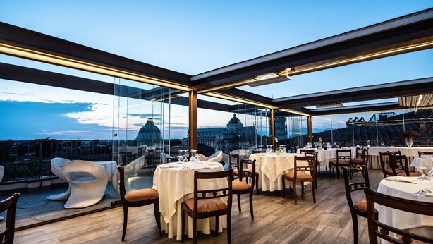 A rooftop restaurant with tables set for dining, overlooking a cityscape with domed buildings. - Grand Hotel Duomo (Pisa)