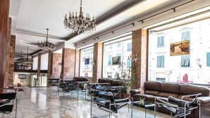 A spacious lobby with leather sofas, metal-framed chairs, and a large chandelier. - Grand Hotel Duomo (Pisa)