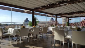 An outdoor dining area with tables and chairs, large windows offering views of historic buildings. - Grand Hotel Duomo (Pisa)