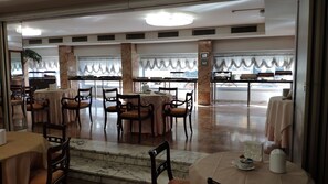 A restaurant with marble-topped tables and chairs, large windows with curtains, and a view of the street outside.