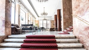 A grand lobby with marble columns, a chandelier, and a staircase with red carpeted steps. - Grand Hotel Duomo (Pisa)