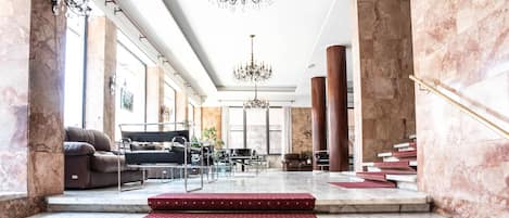 Un amplio vestíbulo con columnas de mármol, un candelabro y una escalera con peldaños alfombrados en rojo.