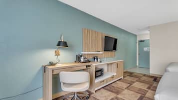Une chambre d’hôtel avec un bureau en bois, une chaise blanche, un téléviseur à écran plat fixé au mur, un four à micro-ondes et un lit.