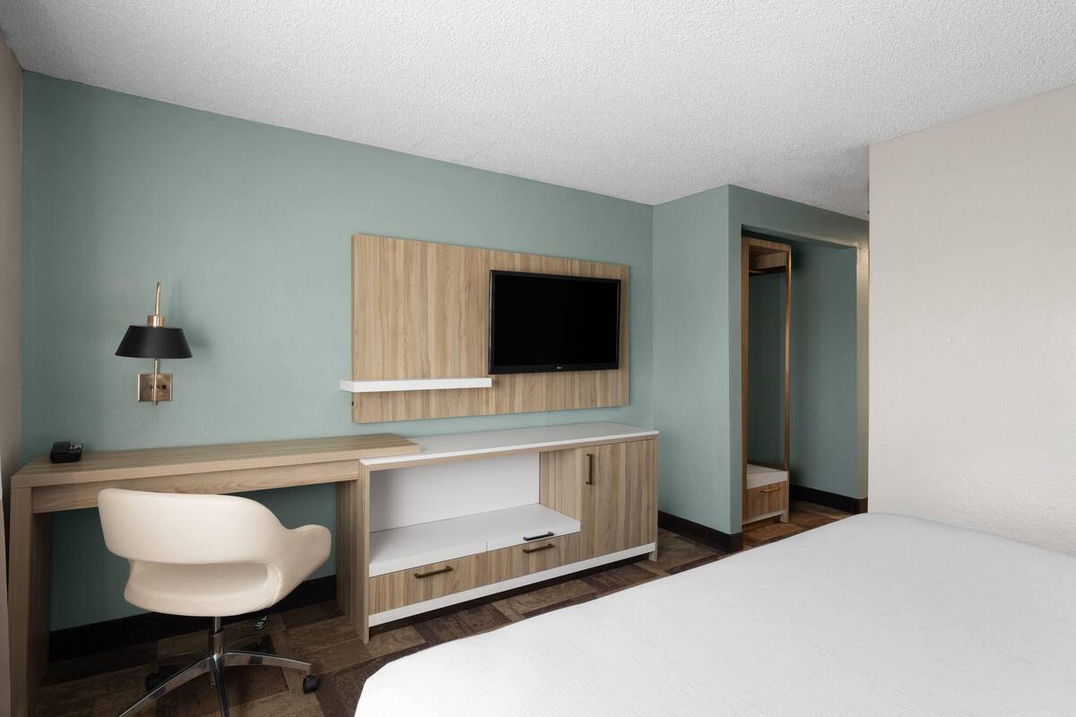 Ein Hotelzimmer mit Bett, Schreibtisch mit Stuhl, einem an der Wand montierten Fernseher und einem Kleiderschrank.