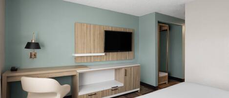 Une chambre d’hôtel comprenant un lit, un bureau avec une chaise, un téléviseur fixé au mur et une armoire.