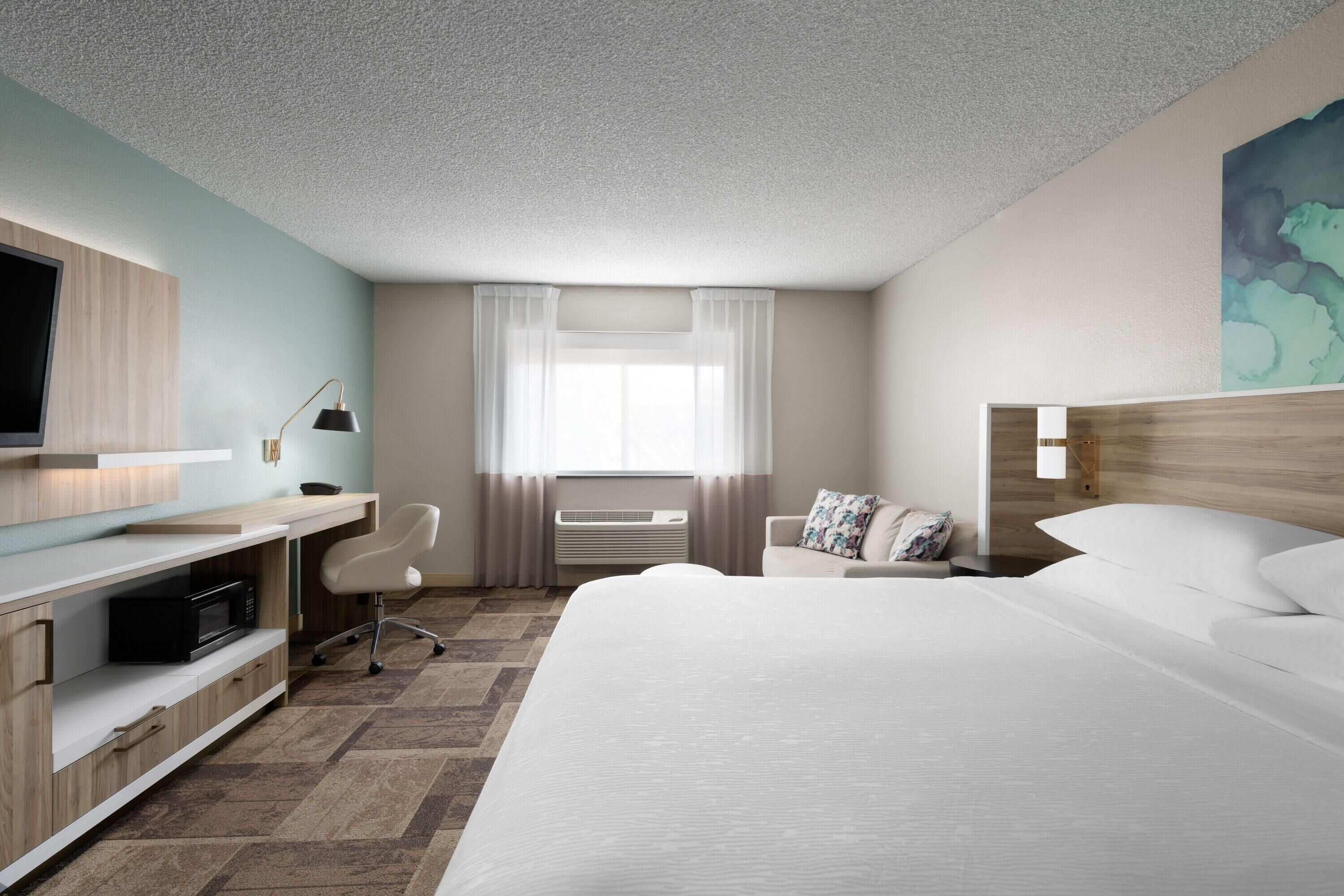Habitación de hotel con cama, escritorio, silla, televisor y una obra de arte en la pared.