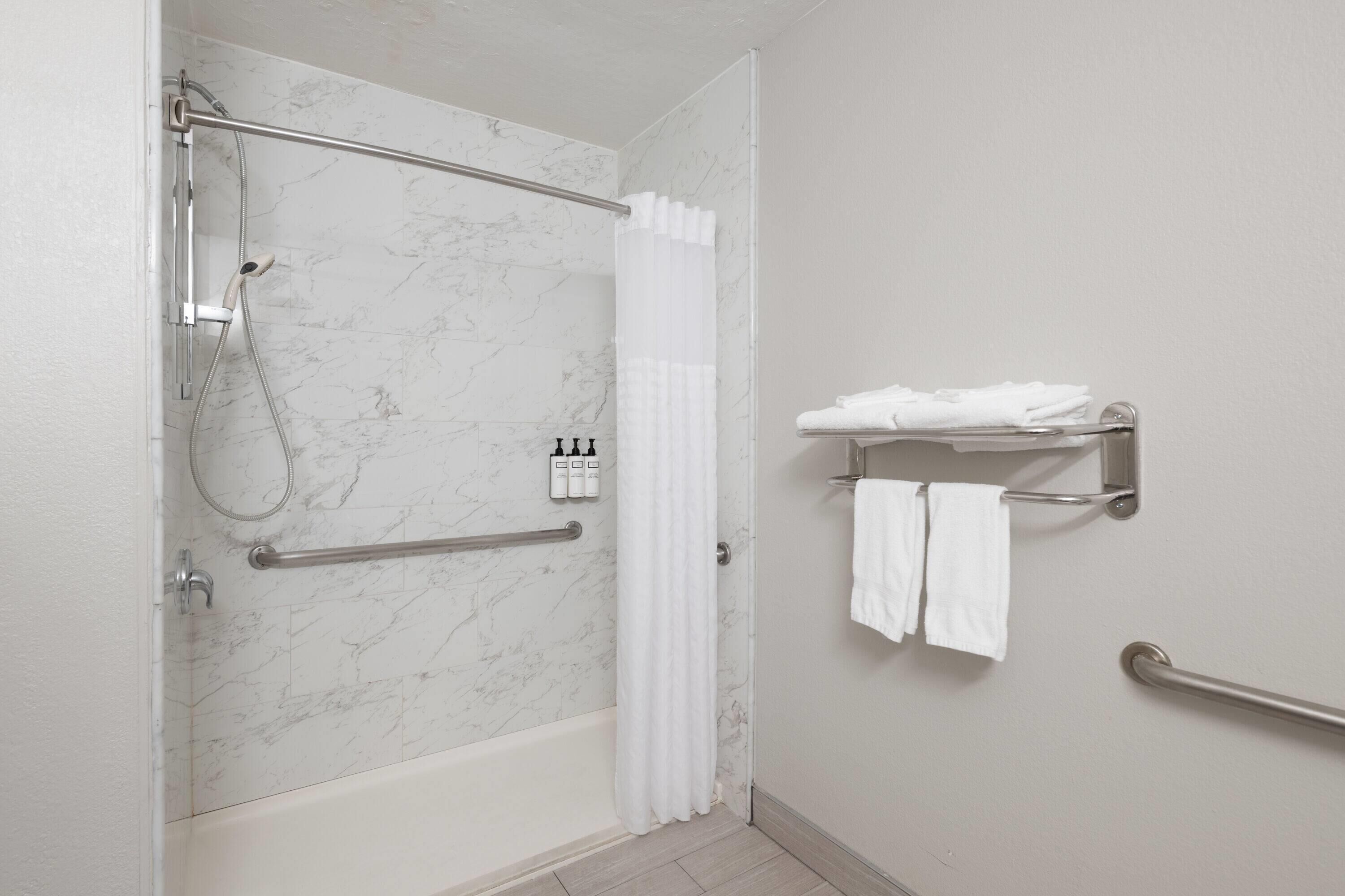 A bathroom with a shower, grab bars, a towel rack, and a marble wall.