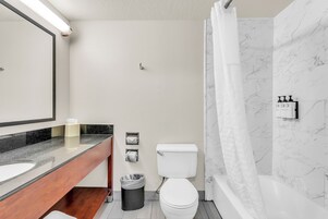 Un baño moderno con pared de mármol, inodoro blanco, tocador de madera, espejo y cortina de ducha.