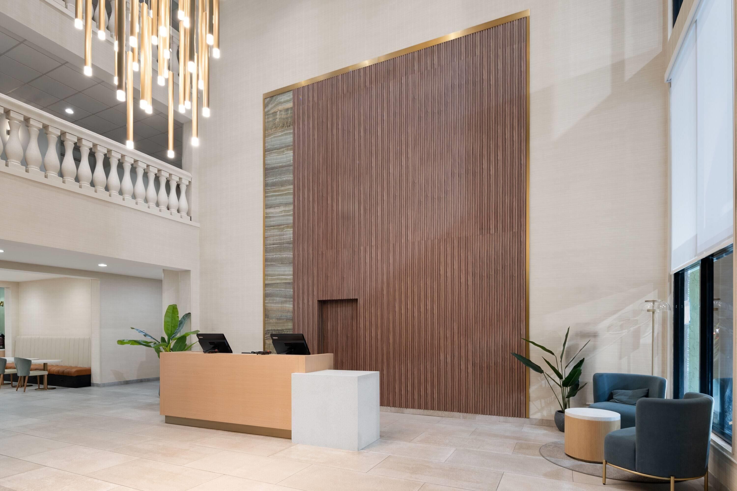 A modern reception area with a wooden panel wall, a reception desk, a seating area with a bench, and a large window providing natural light.