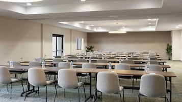 A conference room with rows of tables and chairs, water bottles, and a large plant.