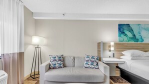 Een hotelkamer met een bank, nachtkastje, lamp, bed en een schilderij aan de muur.