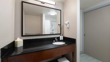 Un baño con encimera negra, lavabo blanco, un espejo grande, dispensador de toallas y barra para toallas.