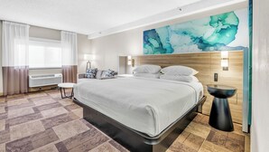 Een moderne hotelkamer met een groot bed, een kunstwerk aan de muur, een nachtkastje en een raam met gordijnen.