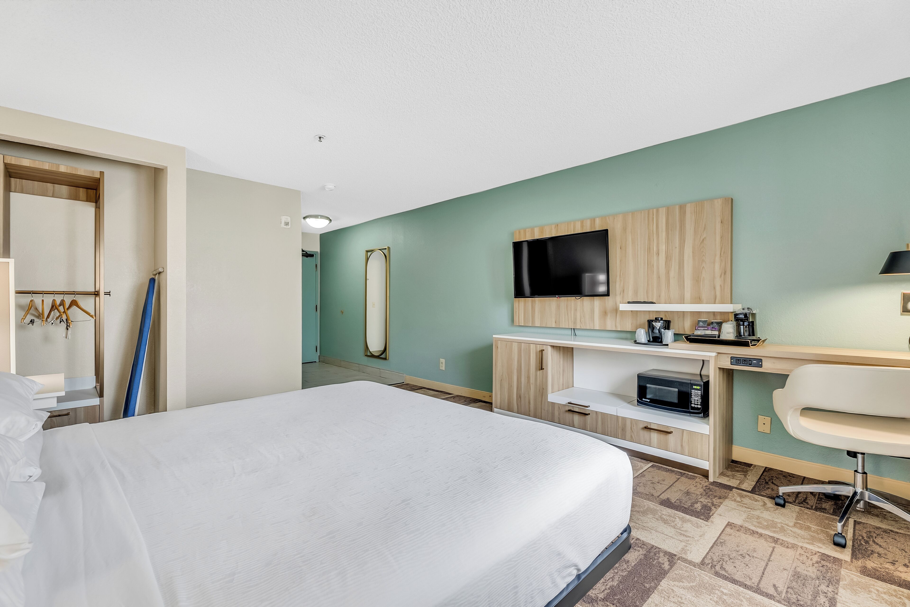 Een hotelkamer met een bed, een bureau met een flatscreen televisie, een magnetron en een stoel.