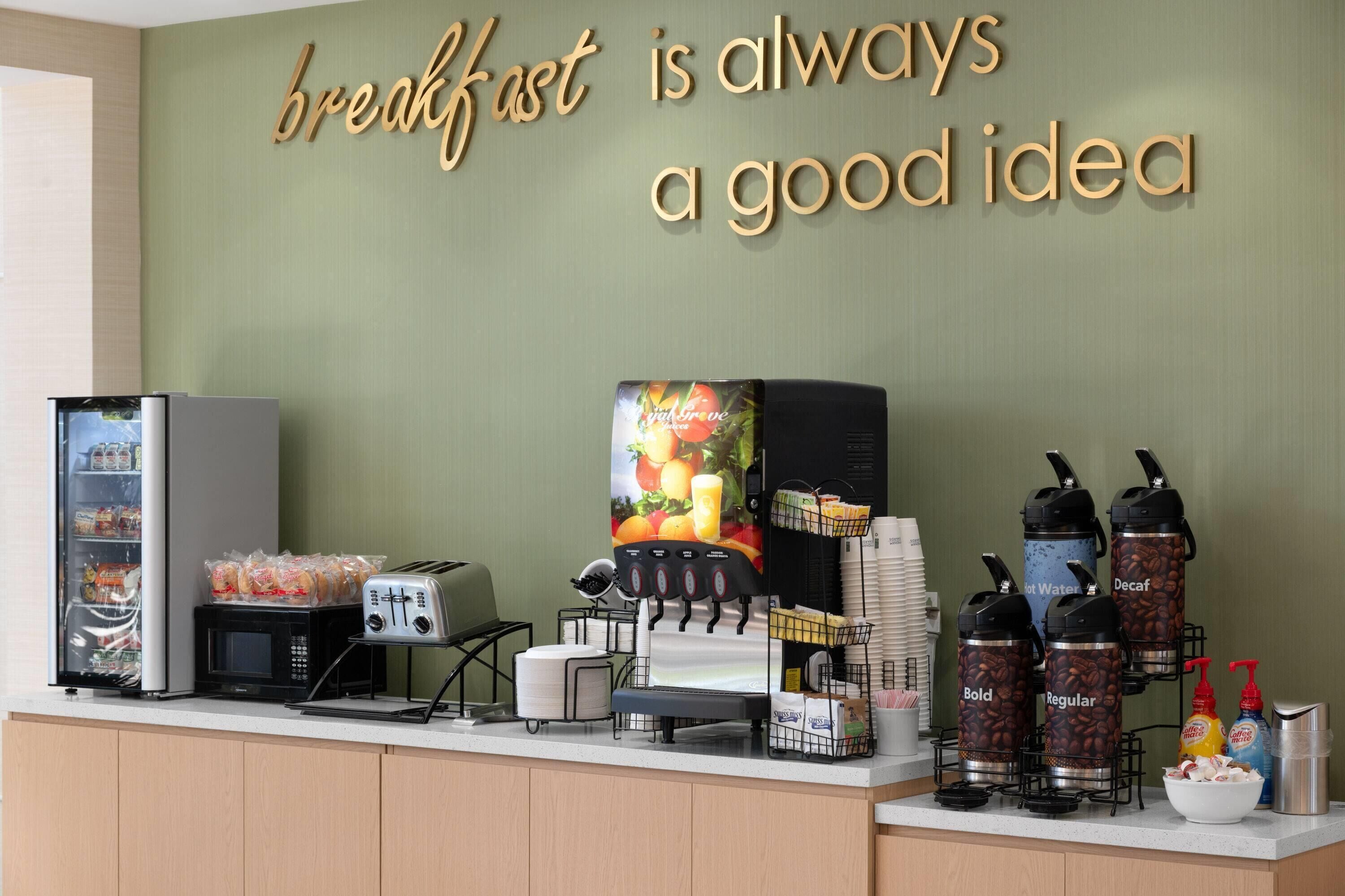 Una barra de desayuno con un cartel que dice “el desayuno siempre es buena idea”, un microondas, tostadora y dispensadores de café.