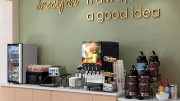 Una barra de desayuno con un cartel que dice “el desayuno siempre es buena idea”, un microondas, tostadora y dispensadores de café.