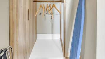 Een kleine kamer met een houten garderobe, een wit schap en een blauw surfplank tegen de muur.