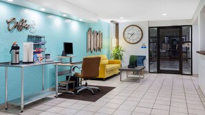 A reception area with a coffee station, a desk, a yellow sofa, and a clock on the wall. - Days Inn by Wyndham Raleigh Glenwood-Crabtree (Raleigh)