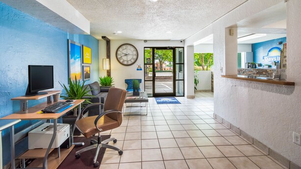 A reception area with a desk, computer, chair, clock, and a door leading outside. - Days Inn by Wyndham Raleigh Glenwood-Crabtree (Raleigh)