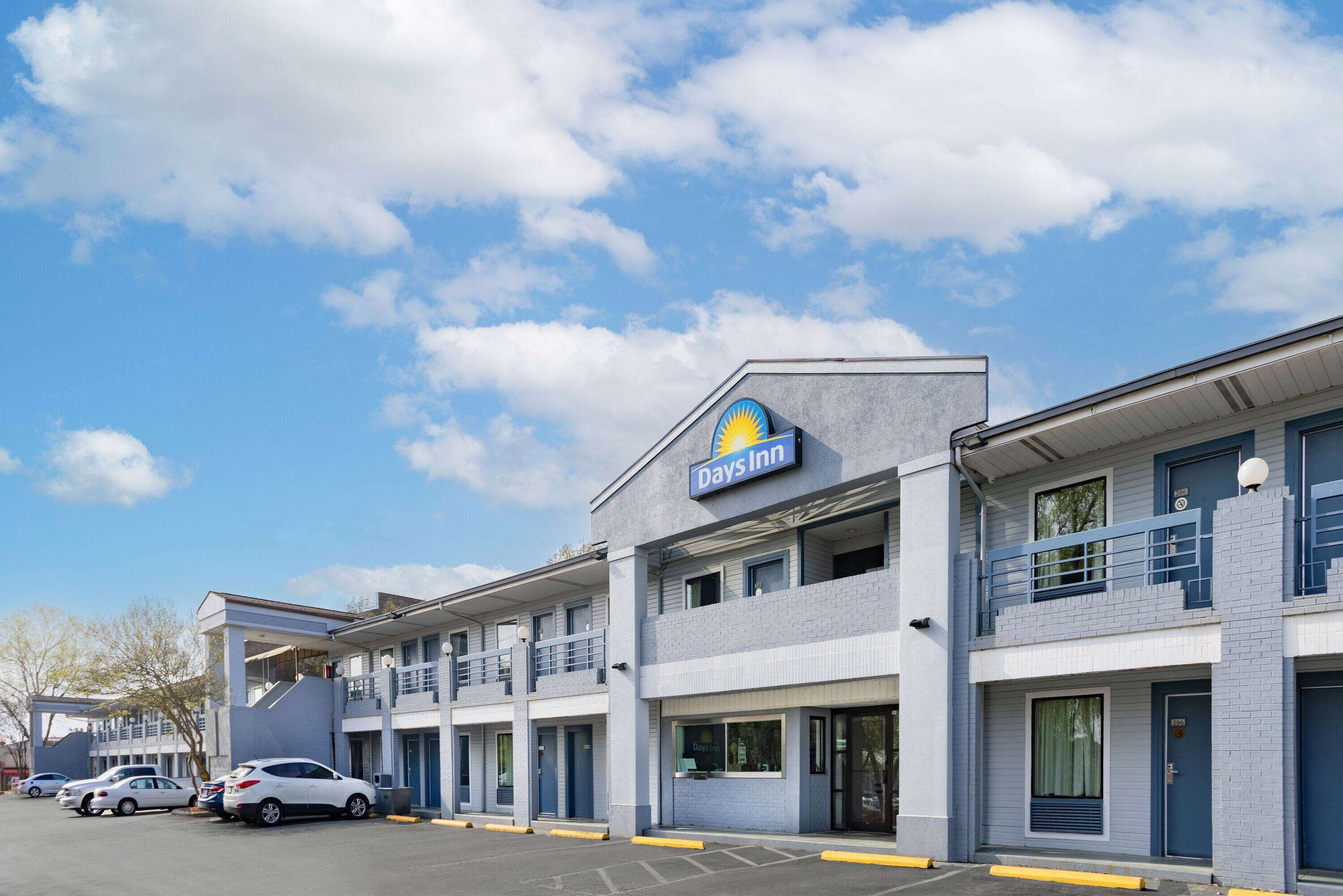 A Days Inn with a clear blue sky and clouds. There are several cars parked in front.